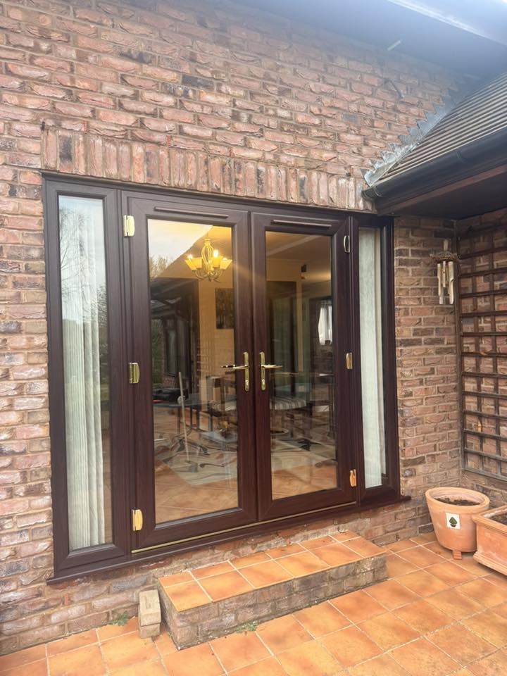 Dark UPVC French patio doors opening from a brick conservatory onto a terracotta patio
