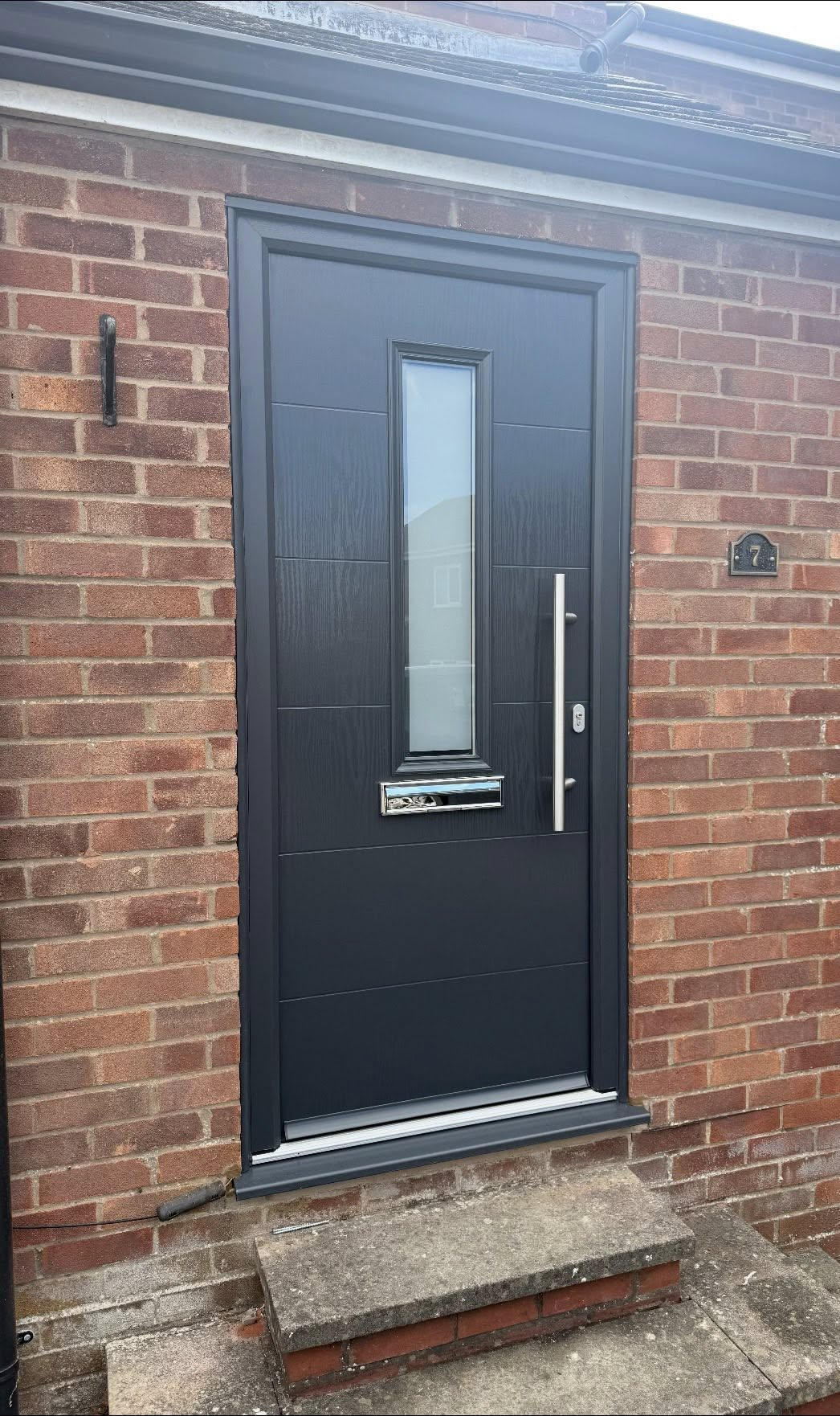 Anthracite grey composite front door with chrome bar handle and letterplate on a red-brick Ludlow home